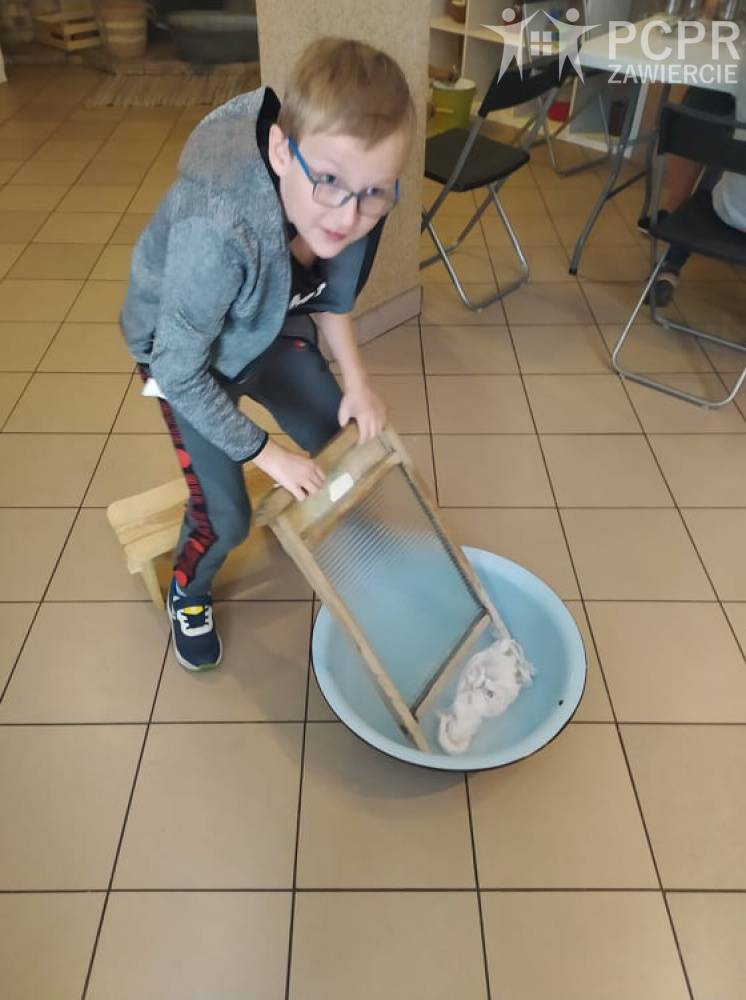 Zdjęcie: Chłopiec pochyla się nad miską trzymając w dłoni tarę do prania